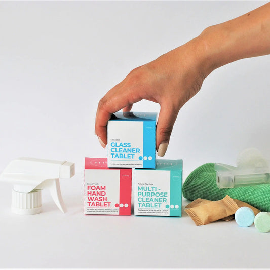 Hand holding 3 cleaning tablet box, with cleaning tablets and spray bottle on the side